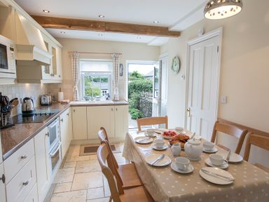 A kitchen with a dining table set for tea and an open door leading to a garden at Jot Cottage in Salcombe