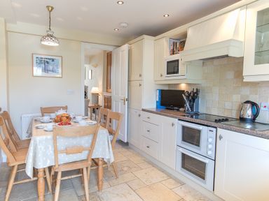 A kitchen with a dining table set for breakfast and white cabinets with appliances at Jot Cottage in Salcombe