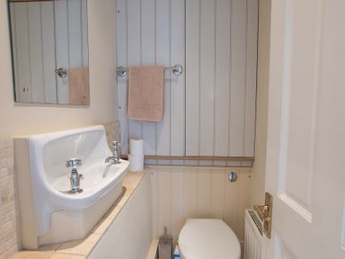 A small bathroom with a wall-mounted sink a mirror a towel on a rack and a toilet at Jot Cottage in Salcombe