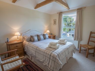 A bedroom with a double bed bedside tables and lamps a window with curtains and wooden chairs at Jot Cottage in Salcombe