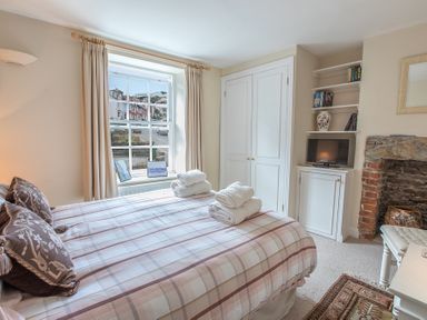 A bedroom with a bed with folded towels near a window and built in shelves with a television at Jot Cottage in Salcombe