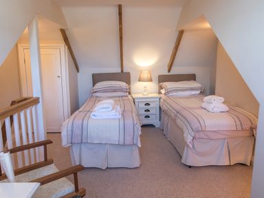 A bedroom with two single beds with linens and folded towels a bedside table with a lamp and a wooden chair at Jot Cottage in Salcombe