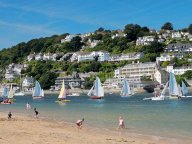 A beach with children playing near the water and sailboats on the sea with houses on a hillside in the background at Jot Cottage in Salcombe