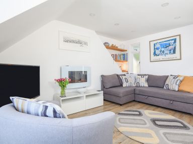 A living room with a gray sectional sofa and armchair a white TV stand with flowers a wall-mounted fireplace and bookshelf at Kings View in Dartmouth