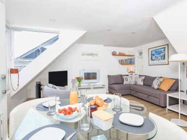 A dining table with food and drinks set up and a living room with a grey sofa and a TV at Kings View in Dartmouth