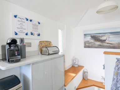 A kitchen corner with a coffee machine on the counter a bread box and a knife holder a wooden stair railing and a painting of a boat on the wall at Kings View Dartmouth