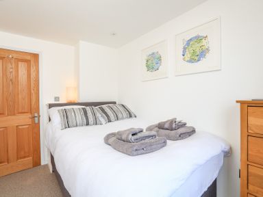 A bedroom with a bed with pillows and folded towels on top two framed pictures on the wall a wooden door and a wooden chest of drawers at Kings View in Dartmouth
