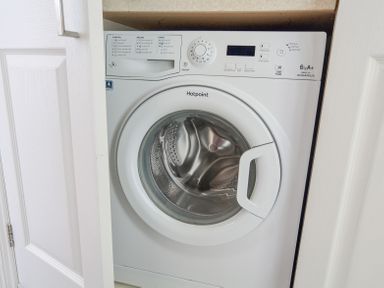 A white front-loading Hotpoint washing machine installed in a cabinet at Kings View in Dartmouth