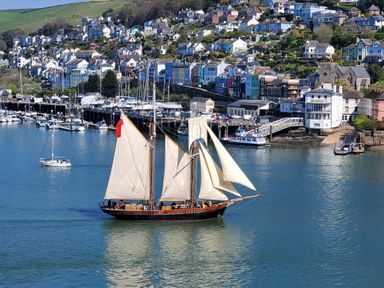 A sailing ship in the water near a harbor with boats and houses on a hillside at Kings View in Dartmouth