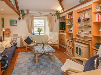 A living room with wooden beams two armchairs a wooden coffee table a window and built in shelves at Lee Shore in Salcombe