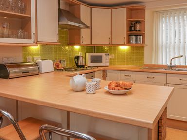 A kitchen with wooden countertop and cabinets a teapot cups and pastries on the counter at Lee Shore in Salcombe