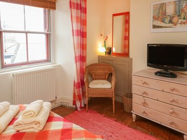 A bedroom with a window chair dresser with a TV and towels on the bed at Lee Shore in Salcombe