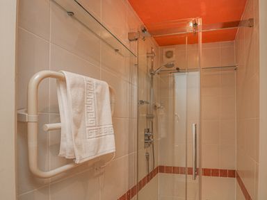 A shower area with glass doors a towel rail with a white towel and tiled walls at Lee Shore in Salcombe