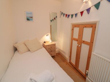 A small bedroom with a single bed a nightstand with a lamp a wall mirror and a small wooden closet at Lee Shore in Salcombe