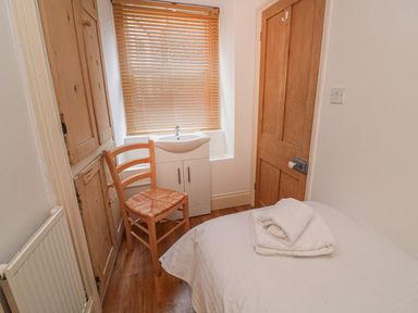 A small bedroom with a single bed with folded towels a wooden chair a sink under a window with blinds and wooden doors at Lee Shore Salcombe