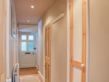 A hallway with a white front door wooden doors coat hooks and a radiator at Lee Shore in Salcombe