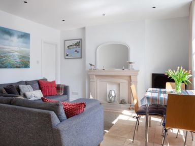 A living room with blue sofas red cushions a fireplace and a dining table with flowers at Lower Fernlea in Salcombe