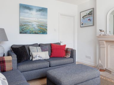A living room with blue sofas and cushions a painting above the sofa and a fireplace at Lower Fernlea in Salcombe