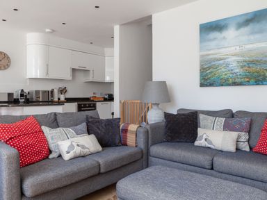 A living area with two grey sofas, patterned throw pillows, a grey lamp, a painting on the wall, and a kitchen in the background at Lower Fernlea in Salcombe