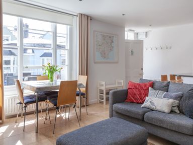 A living room with a grey sofa with patterned cushions a dining table with four chairs and flowers on the table at Lower Fernlea in Salcombe