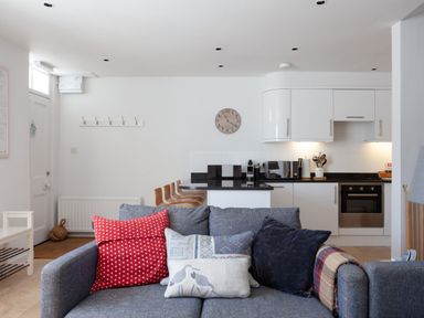 A kitchen area with white cabinets and black countertops and a grey sofa with cushions in Lower Fernlea in Salcombe