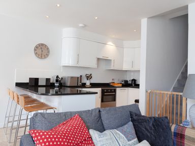 A kitchen with white cabinets black countertops wooden stools and a couch with pillows at Lower Fernlea in Salcombe