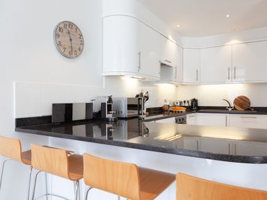 A modern kitchen with a black countertop and wooden bar stools at Lower Fernlea in Salcombe