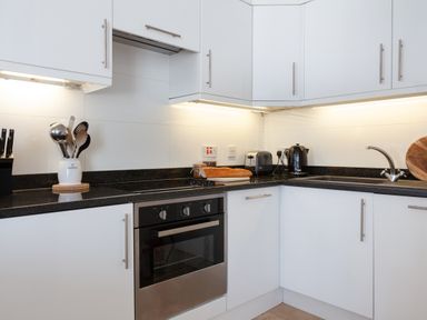 A kitchen corner with white cabinets black countertop oven utensils toaster and kettle at Lower Fernlea in Salcombe
