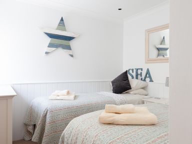 A bedroom with two single beds towels on the beds a large star decoration on the wall and a sea sign at Lower Fernlea in Salcombe