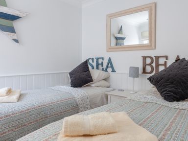 A bedroom with two single beds a bedside table with lamp and decorative letters on the wall at Lower Fernlea in Salcombe