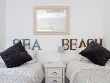A bedroom with two single beds separated by a white nightstand with a lamp and a mirror on the wall at Lower Fernlea in Salcombe