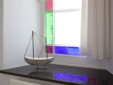 A decorative boat model on a black countertop near a window with colored glass at Lower Fernlea in Salcombe