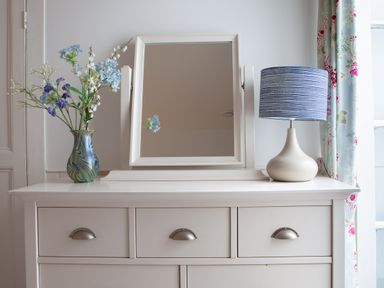 A white dresser with a mirror a blue striped lamp and a vase with flowers at Lower Fernlea in Salcombe