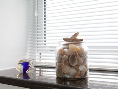 A windowsill with a glass jar filled with seashells and a starfish and a blue and gold glass fish figurine at Lower Fernlea in Salcombe