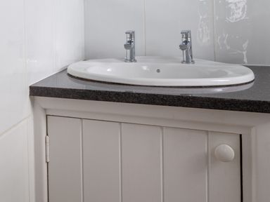 A bathroom sink with two faucets on a black countertop with a white cabinet below at Lower Fernlea in Salcombe