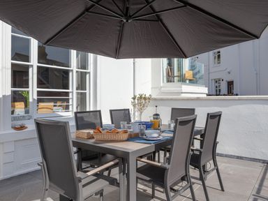 An outdoor patio dining area with a table set with croissants juice bowls and glasses under a large umbrella at Lower Fernlea in Salcombe