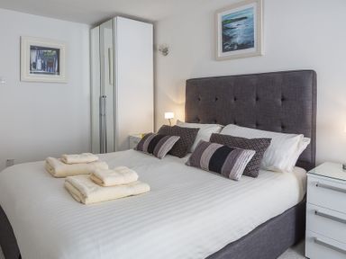 A bedroom with a double bed with pillows and folded towels on it a wardrobe and a bedside table with a lamp at Leeside in Dartmouth