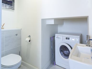 A bathroom with a toilet a washing machine a sink and a folded drying rack at Leeside in Dartmouth