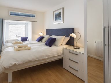 A bedroom with a double bed white bedding and blue pillows beside a white dresser with lamps at Leeside in Dartmouth