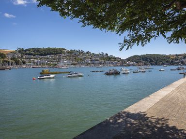 A waterfront with boats anchored in the water and houses on hills in the background at Leeside in Dartmouth