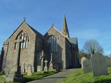 A stone church building with a tall spire and several gravestones in the churchyard at Meadow View in Modbury