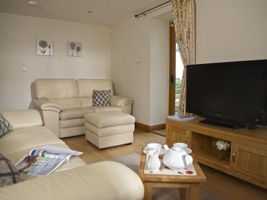 A living room with cream leather sofas a wooden TV stand with a television and a small wooden table with a tea set at Meadow View in Modbury