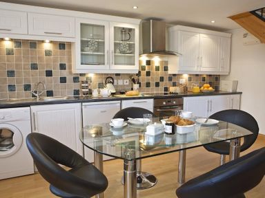 A kitchen with white cabinets dishwasher oven and a glass dining table with black chairs at Meadow View in Modbury