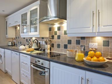 A kitchen with white cabinets tiled backsplash and countertop with oranges and a jug of orange juice at Meadow View in Modbury