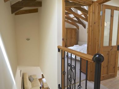 A hallway with wooden beams and a staircase leading down to a living area with a cream sofa and a bedroom with wooden furniture at Meadow View in Modbury