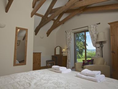 A bedroom with exposed wooden beams a bed with folded towels a mirror a dressing table an armchair and a window showing a landscape at Meadow View in Modbury