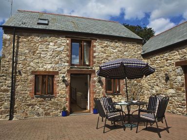 An outdoor patio area with a stone building a table chairs and a large umbrella at Meadow View in Modbury
