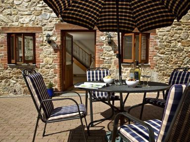 A patio with a round table and striped chairs under a striped umbrella at Meadow View in Modbury