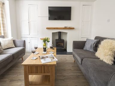 A living room with two grey sofas a wooden coffee table with wine glasses and a bottle and a wall mounted television at The Old Wash House in Dartmouth