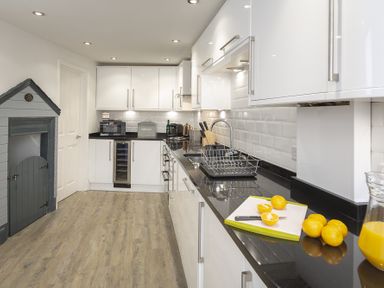 A kitchen with white cabinets and black countertops with oranges on a cutting board and a dog house in the corner at The Old Wash House in Dartmouth